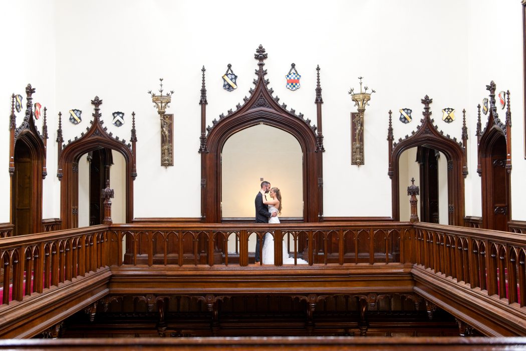 bride and groom holding on to each other romantically, in a castle, arch framing them, groom kissing bride