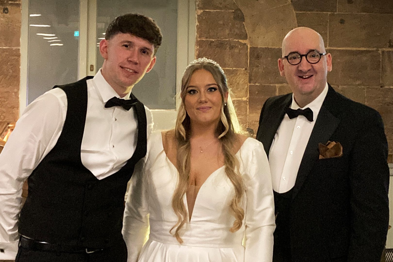 Bride in white dress flanked by two men in black suits
