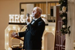 Singer in black tuxedo sings into a vintage style microphone. There are giant light up letters behind him spelling mr and mrs
