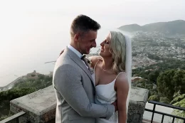 bride and groom look at each other with italian backdrop behind them and the ocean