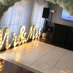 Light-up 'Mr & Mrs' sign with white floral arch at a wedding reception venue
