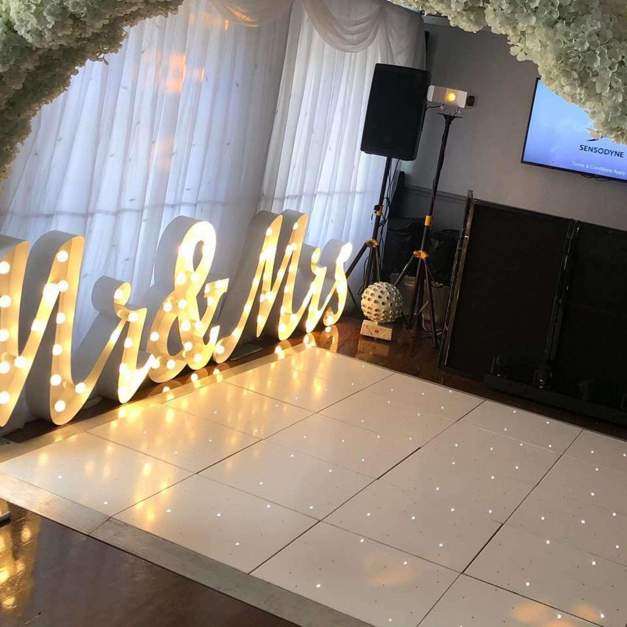 Light-up 'Mr & Mrs' sign with white floral arch at a wedding reception venue