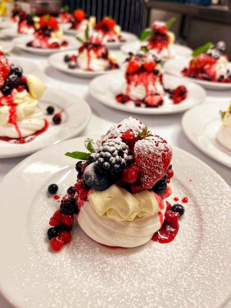 Plated dessert topped with fresh strawberries, blueberries, and a pink fruit sauce