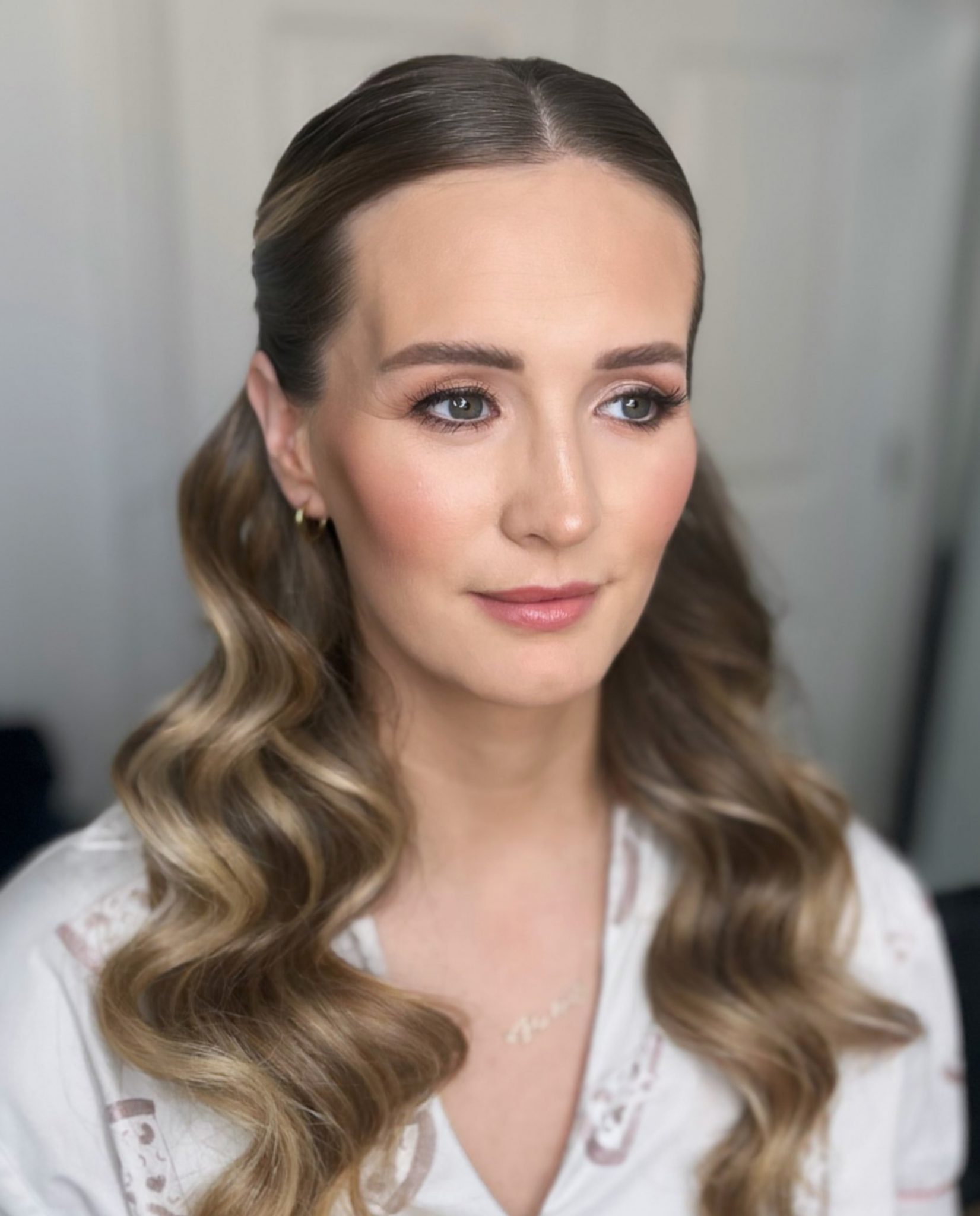 Bride with soft blonde half-up hairstyle featuring loose waves, paired with natural glowy makeup that enhances her features with subtle radiance.