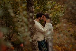 A couple seen through forestry scene kissing by a tree