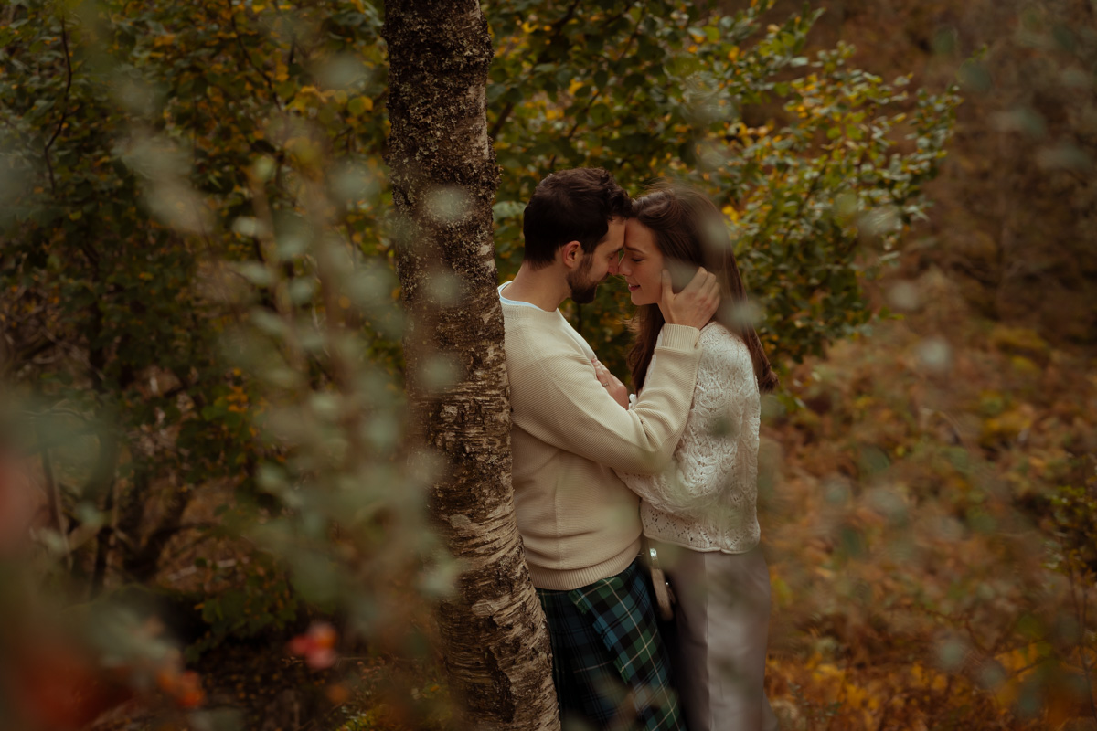 A couple seen through forestry scene kissing by a tree