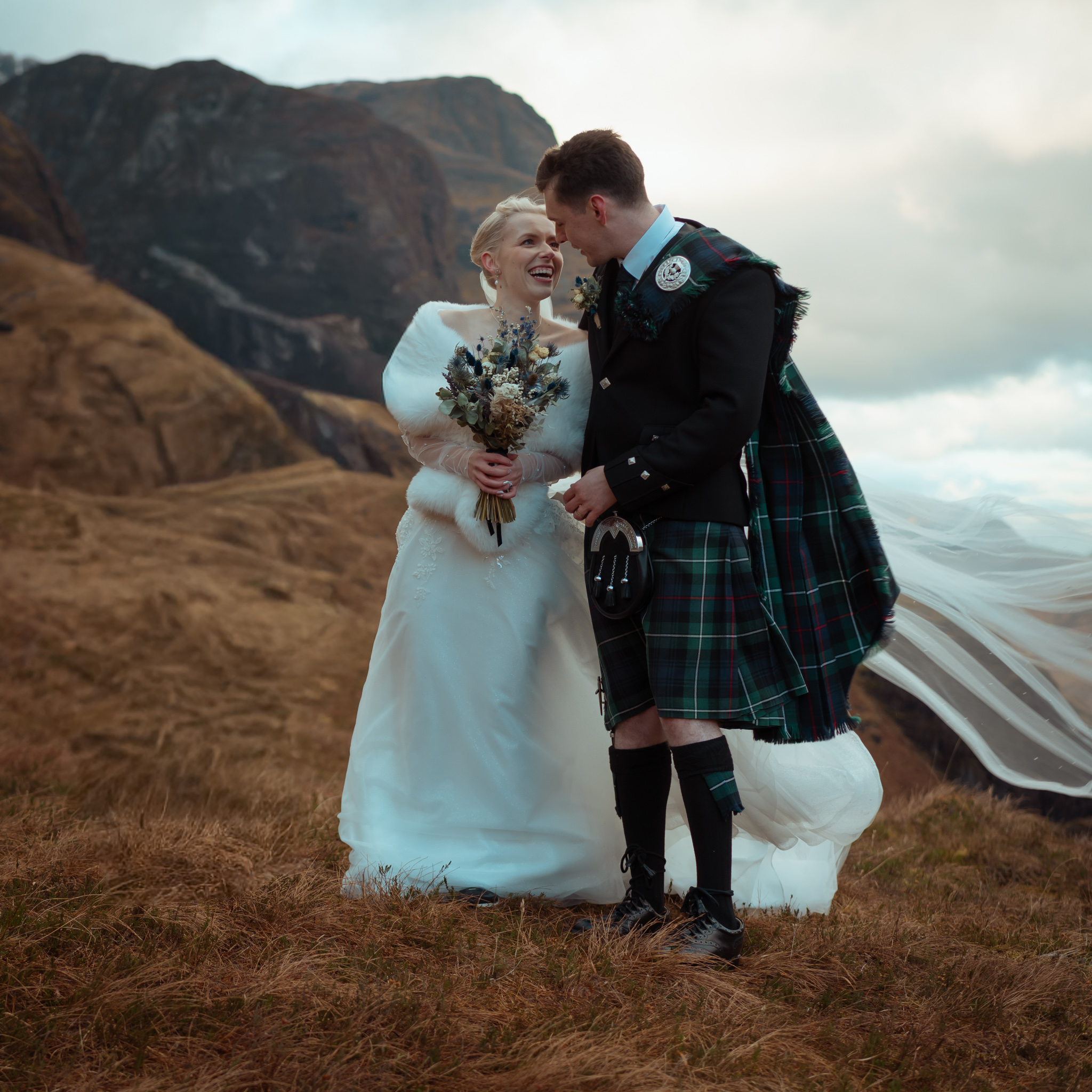 A wedded couple stand on a mountain in Glencoe with the veil caught in the wind