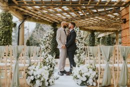 Luxury same-sex wedding styling at The Sun Pavilion by Love Stories Events featuring white floral ceremony meadows, statement wedding arch, romantic aisle flowers, sage green chair draping and elegant outdoor ceremony decor. Yorkshire wedding stylist specialising in luxury wedding decor hire, ceremony styling, floral installations and editorial wedding design for Harrogate weddings, Leeds weddings, York weddings and modern romantic wedding inspiration.