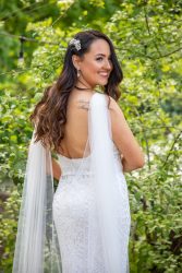 A bride stood in front of some green foliage, smiling and looking over her shoulder.