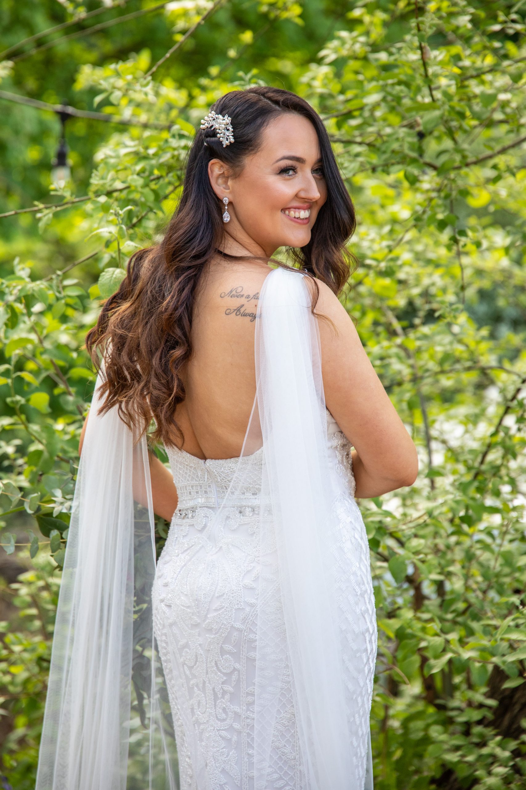 A bride stood in front of some green foliage, smiling and looking over her shoulder.