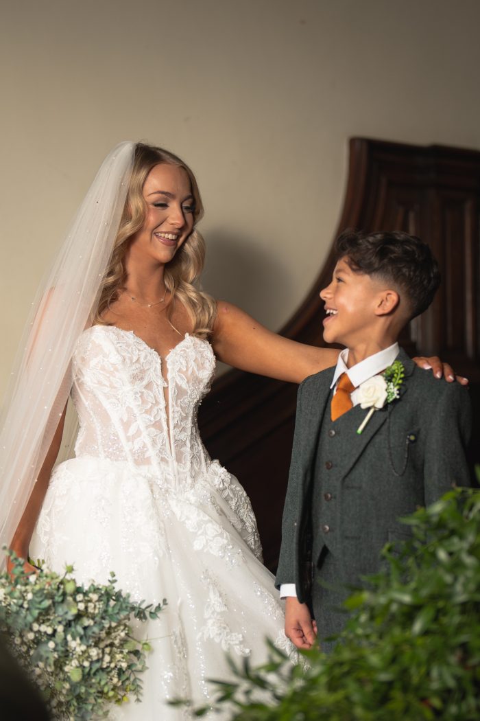 A page boy wearing an olive green tweed wedding suit posing with the bride.
