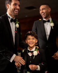 A page boy wearing a black 3-piece tuxedo matching with the groomsmen.
