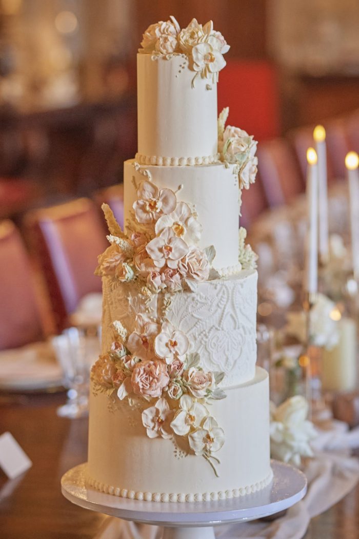 Four-tier white buttercream wedding cake with delicate blush flowers orchids, roses and intricate piped details