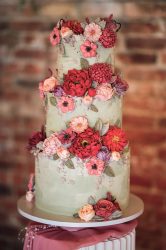 Three-tier sage green buttercream wedding cake decorated with red, coral and pink buttercream flowers