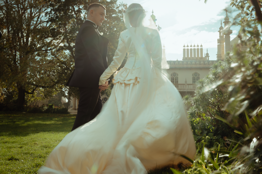 A picture of a wedded couple walking in manor gardens towards a palace